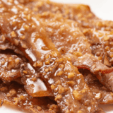 Air fryer praline bacon strips coated in caramelized brown sugar and chopped pecans on parchment paper