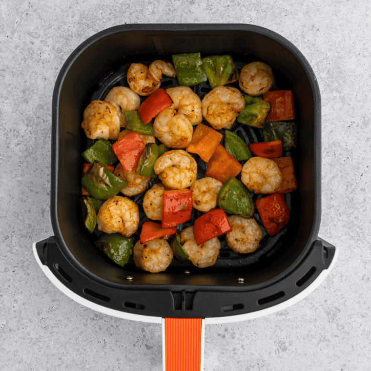 Cooked honey-lime shrimp in a single layer in the air fryer basket, opaque and curled into a loose "C" shape