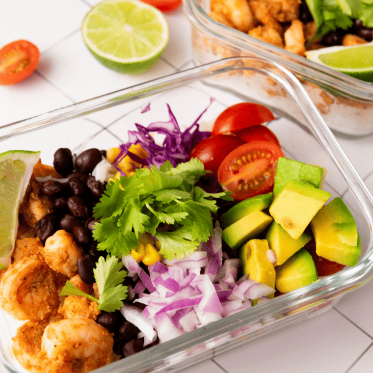 Overhead view of a finished shrimp taco bowl topped with shrimp, diced mango, slaw, pickled onions, and a drizzle of cilantro-lime crema