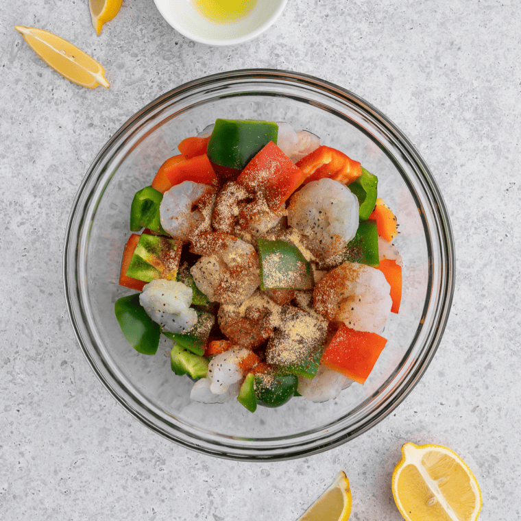 Raw shrimp tossed with honey, lime juice, garlic, and chili powder in a glass mixing bowl