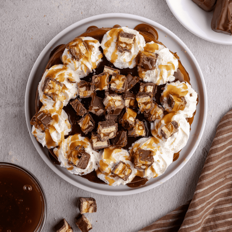 Sliced air fryer Snickers cheesecake topped with caramel drizzle, chopped Snickers, and peanuts