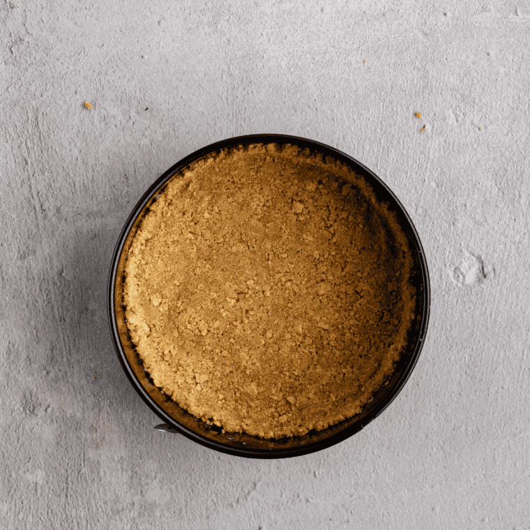 Graham cracker crust pressed into a parchment-lined springform pan for air fryer Snickers cheesecake