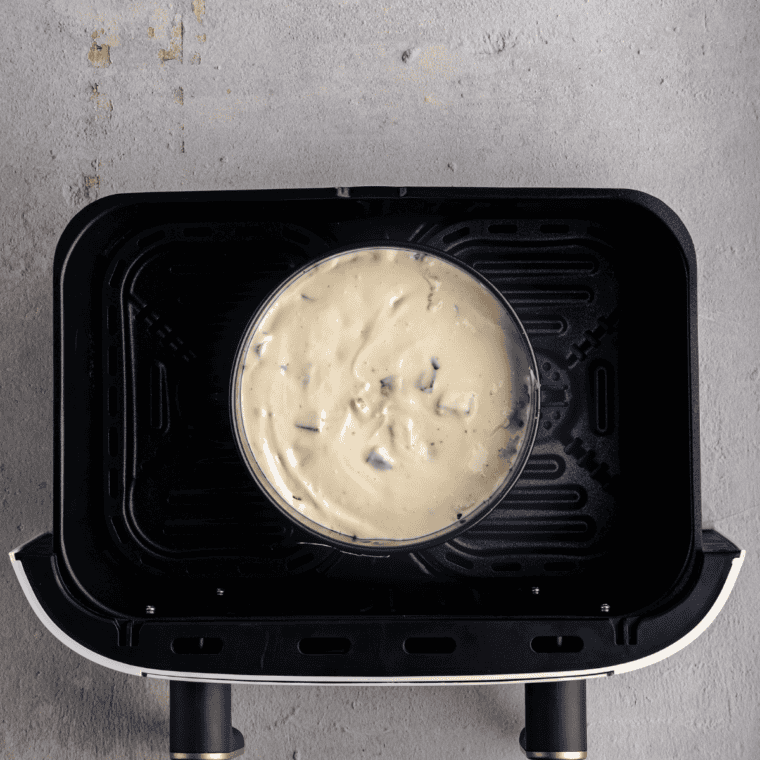 Snickers cheesecake in a springform pan inside the air fryer basket before baking at 300&deg;F