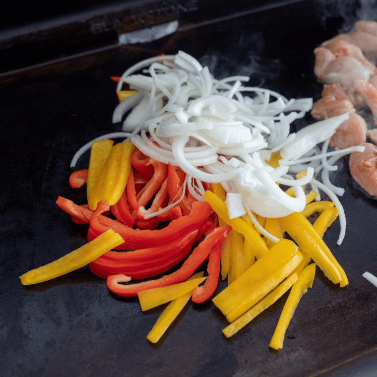 Seasoned chicken strips searing in a single layer on a Blackstone griddle