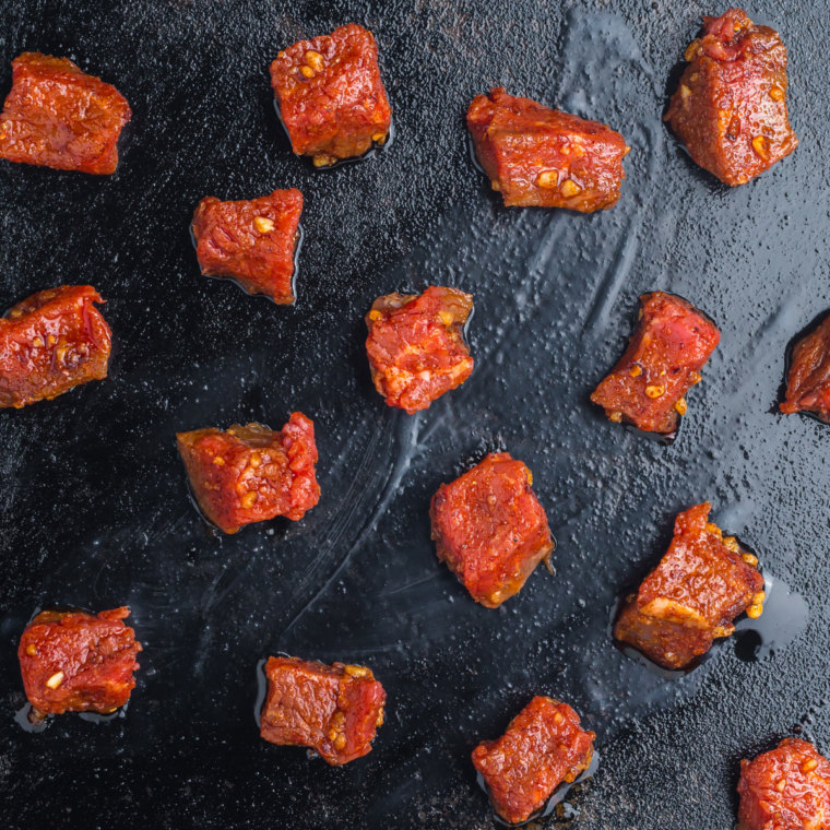 Seasoned steak cubes searing in a single spaced-out layer on a Blackstone griddle