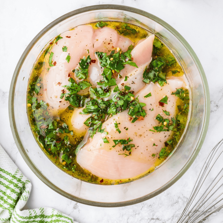 Raw chicken breasts marinating in copycat Lawry's lemon pepper marinade with fresh lemon slices