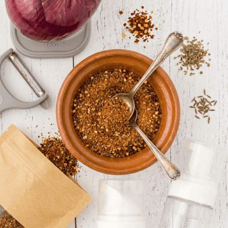 Spice blend ingredients including chili powder, cumin, paprika, salt, garlic powder, onion powder, oregano, black pepper, red pepper flakes, cornstarch, and sugar mixed in a small bowl or jar.