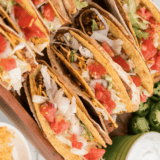 Three crispy Del Taco copycat beef tacos topped with shredded cheddar and lettuce on a plate
