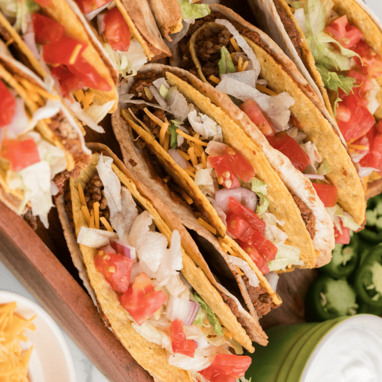 Three crispy Del Taco copycat beef tacos topped with shredded cheddar and lettuce on a plate