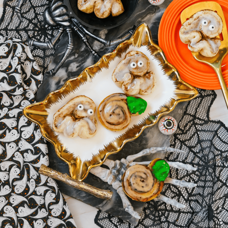 Halloween cinnamon rolls decorated as orange pumpkins and white ghosts on a tray.