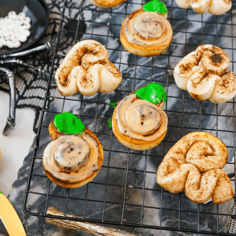 Pumpkin cinnamon rolls frosted with orange icing and green stems for Halloween.