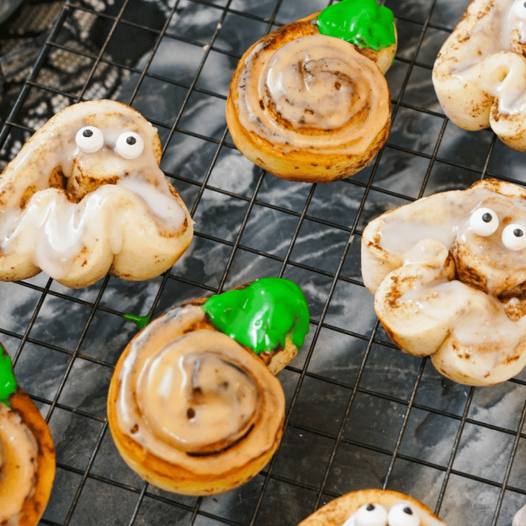 Ghost Halloween cinnamon rolls frosted white and topped with candy eyes.