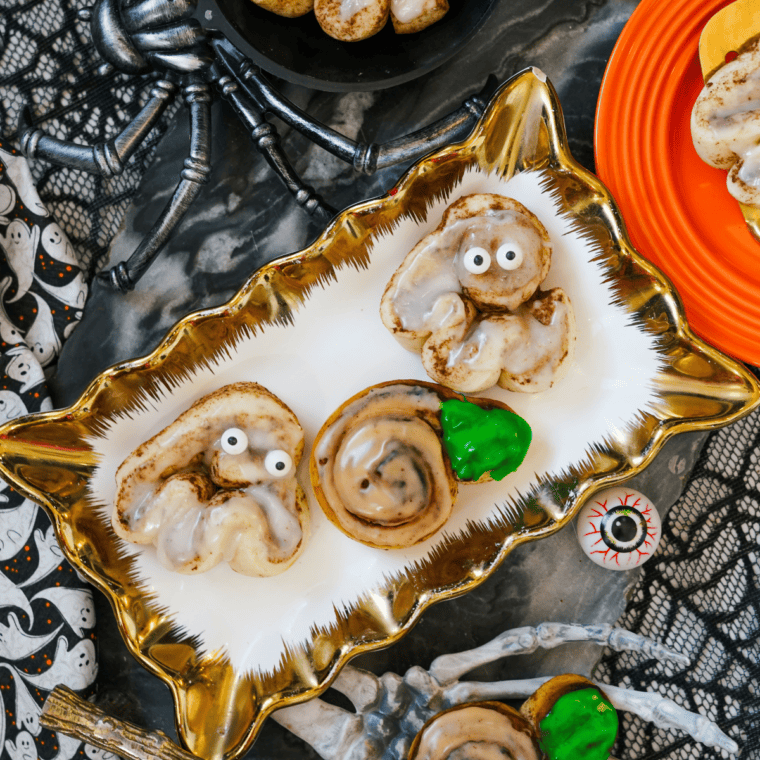 Halloween cinnamon rolls decorated as orange pumpkins and white ghosts on a tray.