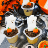 Halloween pudding cups topped with candy pumpkins, ghost Peeps, and crushed chocolate cookie crumbs