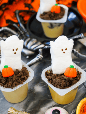 Halloween pudding cups topped with candy pumpkins, ghost Peeps, and crushed chocolate cookie crumbs