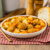 Bowl of slow cooker meatball vegetable soup with potatoes, carrots, and green beans, topped with fresh parsley