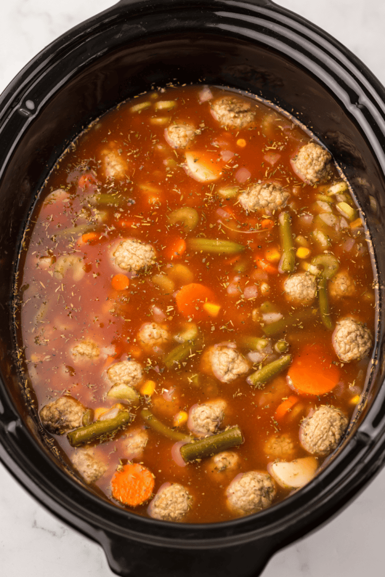 Pouring tomato sauce and broth over meatballs and vegetables in a slow cooker, then adding seasonings