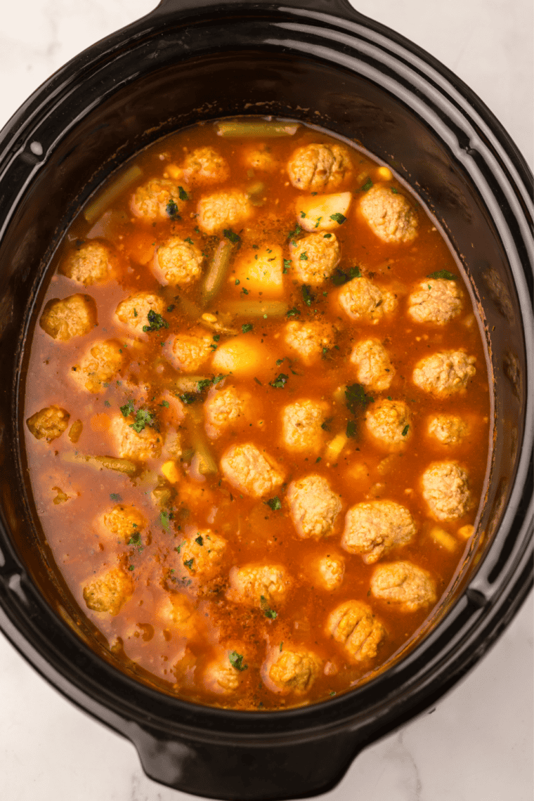 Slow cooker covered with lid to cook meatball vegetable soup until the vegetables are tender