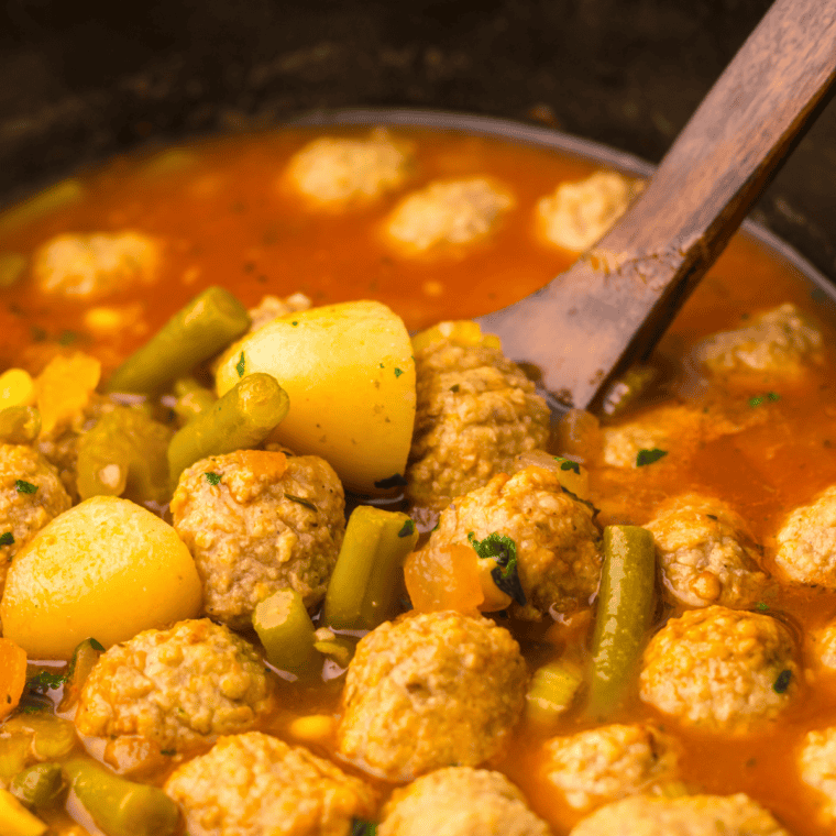 Covered slow cooker cooking meatball vegetable soup on low until tender