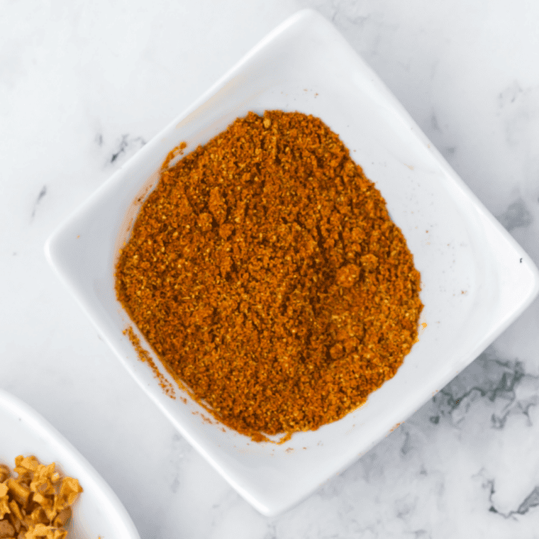 Homemade curry powder recipe in a white bowl with a wooden spoon