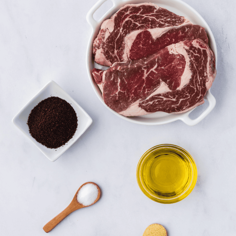 Jack Daniel's rib eye steak ingredients laid out, including ribeye steaks, whiskey, soy sauce, brown sugar, garlic, and butter