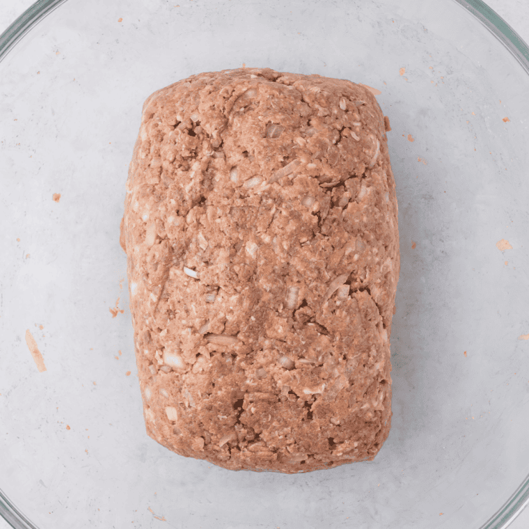 Raw meatloaf shaped into a free-form loaf on a parchment-lined sheet pan