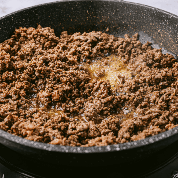 Ground beef browning in a large skillet over medium high heat, with rich caramelized bits forming on the bottom of the pan to build flavor for a quick homemade chili recipe.