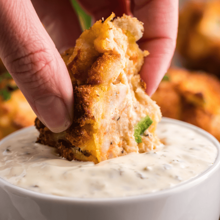 Hand dipping a crispy hush puppy into a bowl of homemade mayonesa con lim&oacute;n