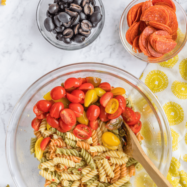 tossing pasta and vegetables with italian dressing and salad supreme seasoning in large bowl