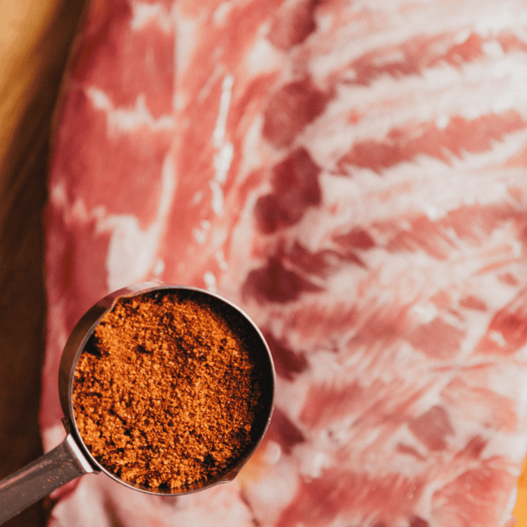 Copycat Meat Church Honey Hog BBQ rub being applied to a rack of raw pork ribs