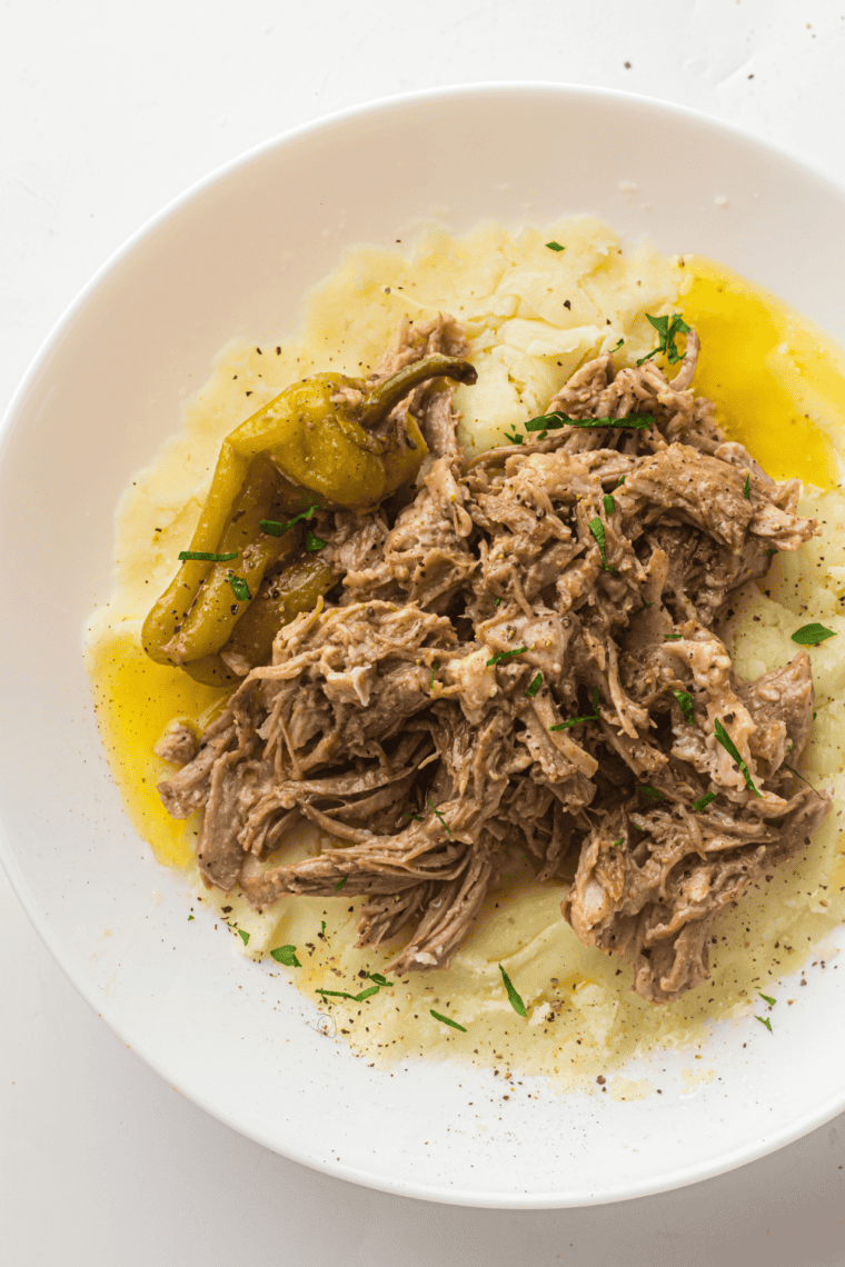 Slow Cooker Mississippi Pork Roast served on a platter with pepperoncini peppers and savory juices.