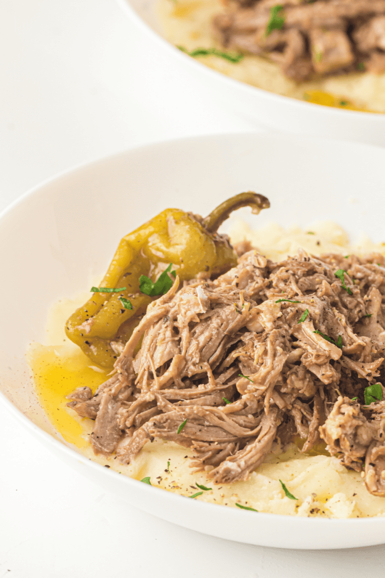 Tender shredded Slow Cooker Mississippi Pork Roast with pepperoncini and buttery au jus in a white crockpot