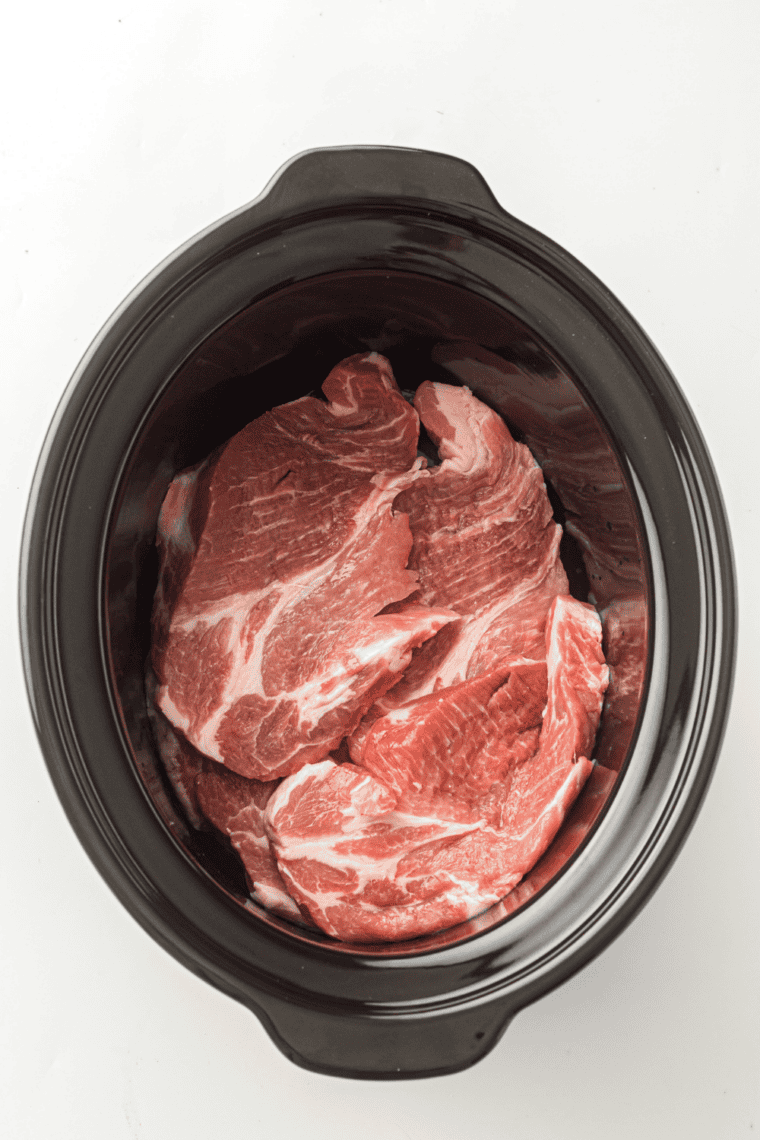 Raw pork shoulder placed in the bottom of a slow cooker for Mississippi Pork Roast