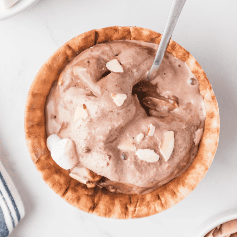 Close-up of a bowl of Ninja Creami copycat Blue Bell Rocky Road showing chocolate, almonds, and marshmallows