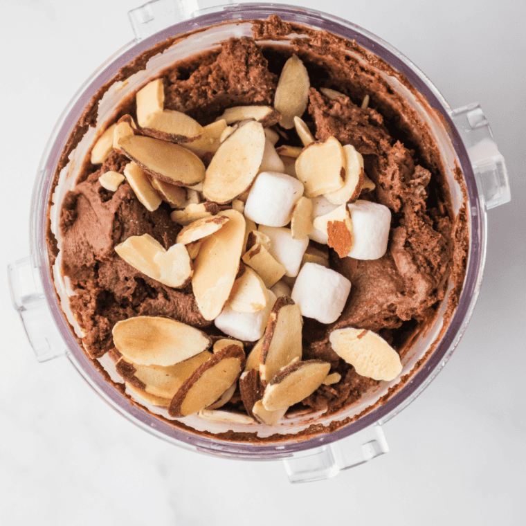 Adding mini marshmallows, almonds, and chocolate chips into a hole in the spun Ninja Creami Rocky Road pint
