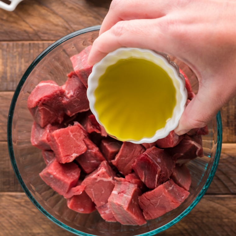 Steak cubes tossed with oil and smoked paprika seasoning in a glass bowl
