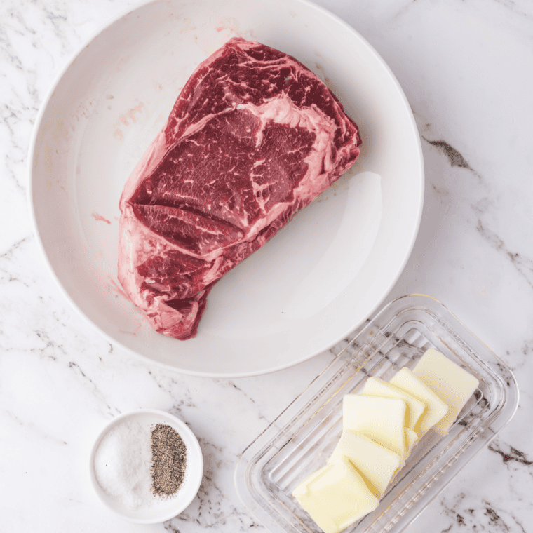 Raw bone-in Cowboy Ribeye steak showing heavy marbling on a wooden cutting board