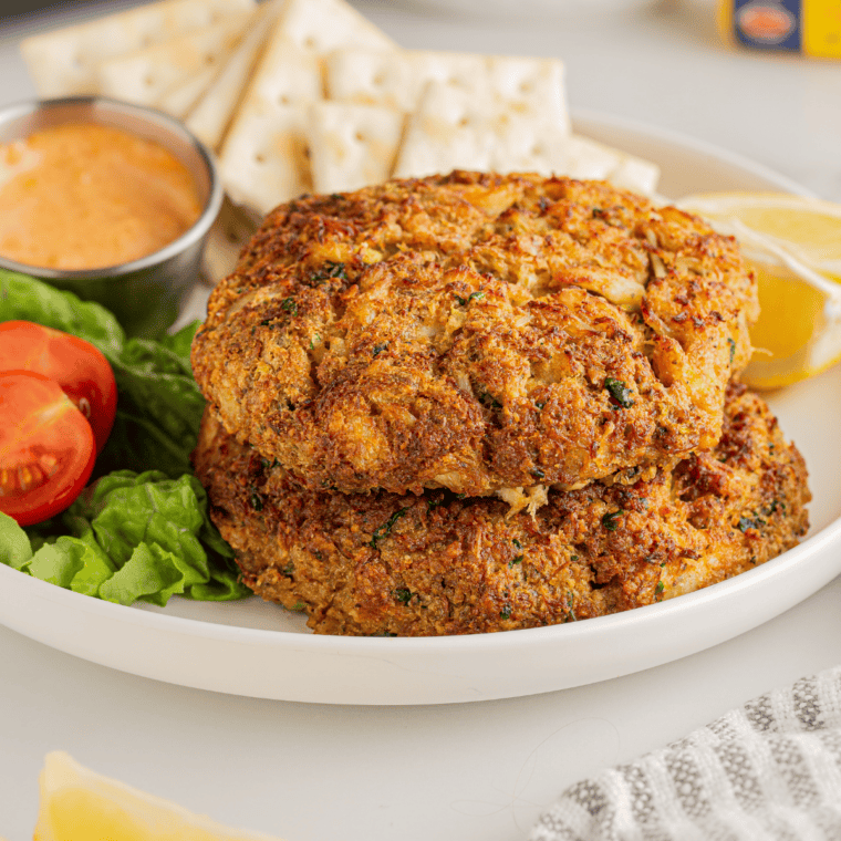 Crab cakes searing golden brown in butter in a skillet.
