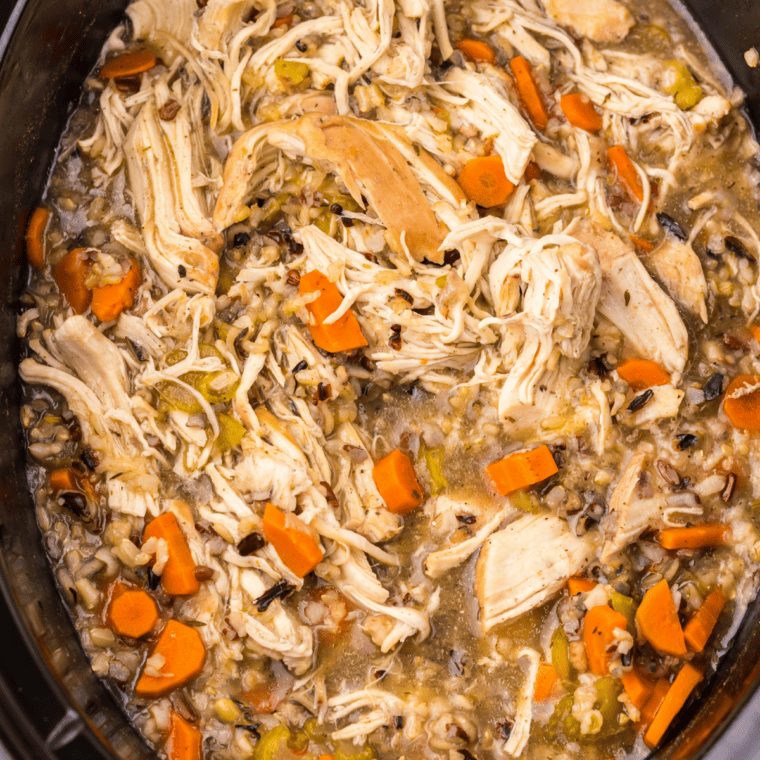Cooked chicken being shredded with two forks on a cutting board