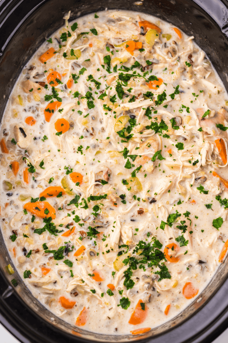 Bowl of creamy slow cooker chicken and wild rice soup with carrots and celery, served with crusty bread