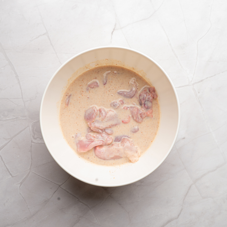 Thin chicken patties soaking in buttermilk and hot sauce marinade before breading