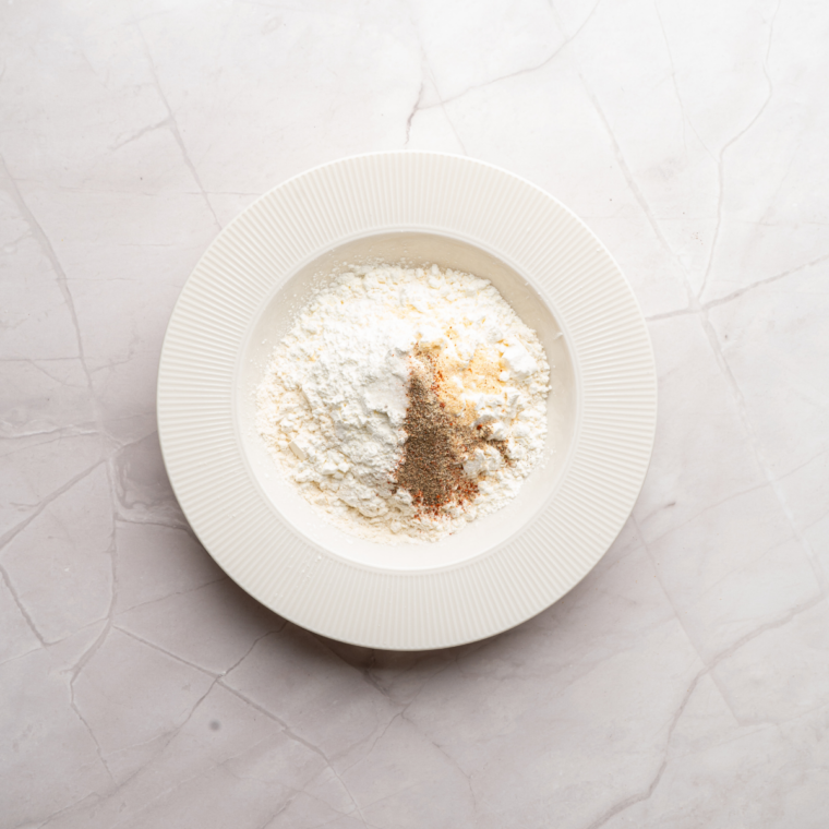 Double-dredging a chicken patty in seasoned flour to build a crispy, craggy coat