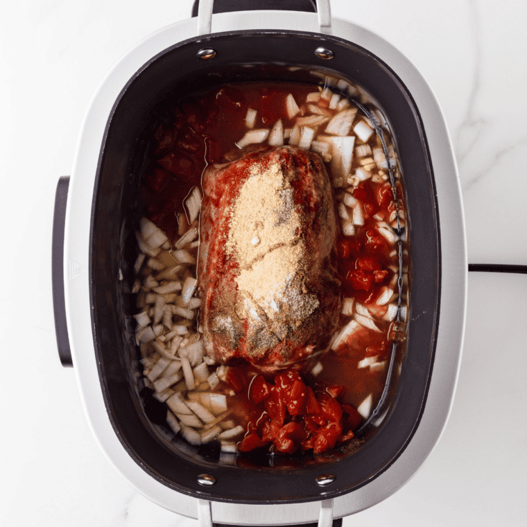 Seasoned pork shoulder placed over sliced onion and garlic in a slow cooker