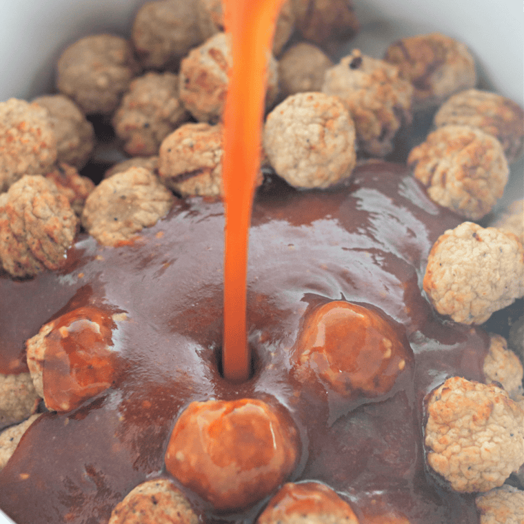 Frozen meatballs being tossed in whiskey BBQ sauce in the crockpot