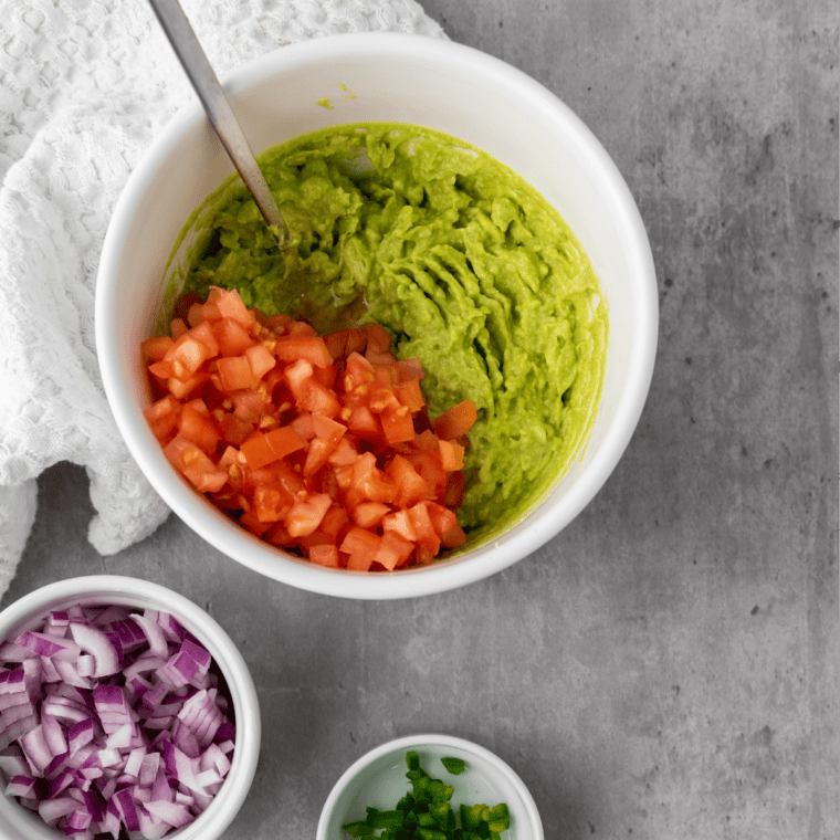 Red onion, tomato, chilli and coriander being folded into mashed avocado in a bowl