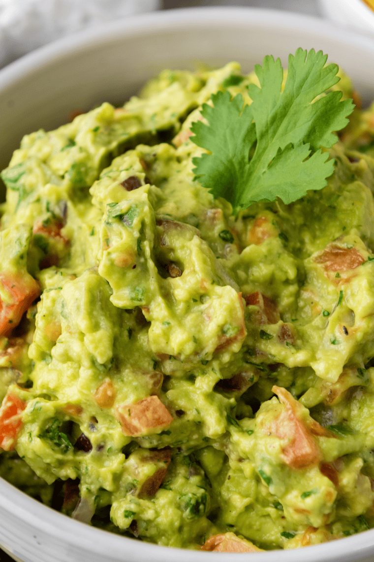 Fresh guacamole topped with coriander and red onion in a white bowl