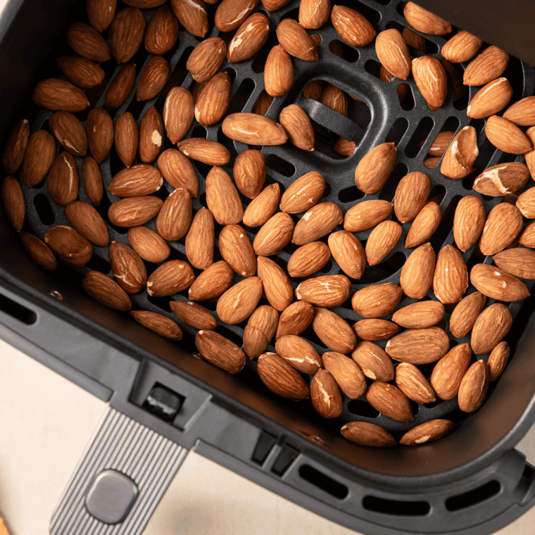 Raw almonds in a single layer in an air fryer basket ready to roast