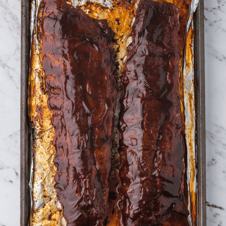 Baby back ribs brushed with barbecue sauce and broiling in the oven