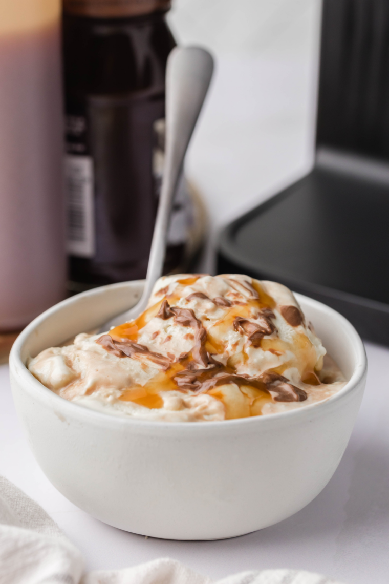 Two scoops of copycat Blue Bell Chocolate Lava Cake ice cream in a white bowl, drizzled with chocolate sundae sauce.