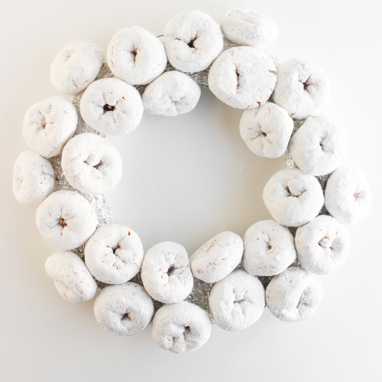  Half-finished donut wreath showing powdered mini donuts attached around one side of the foam form